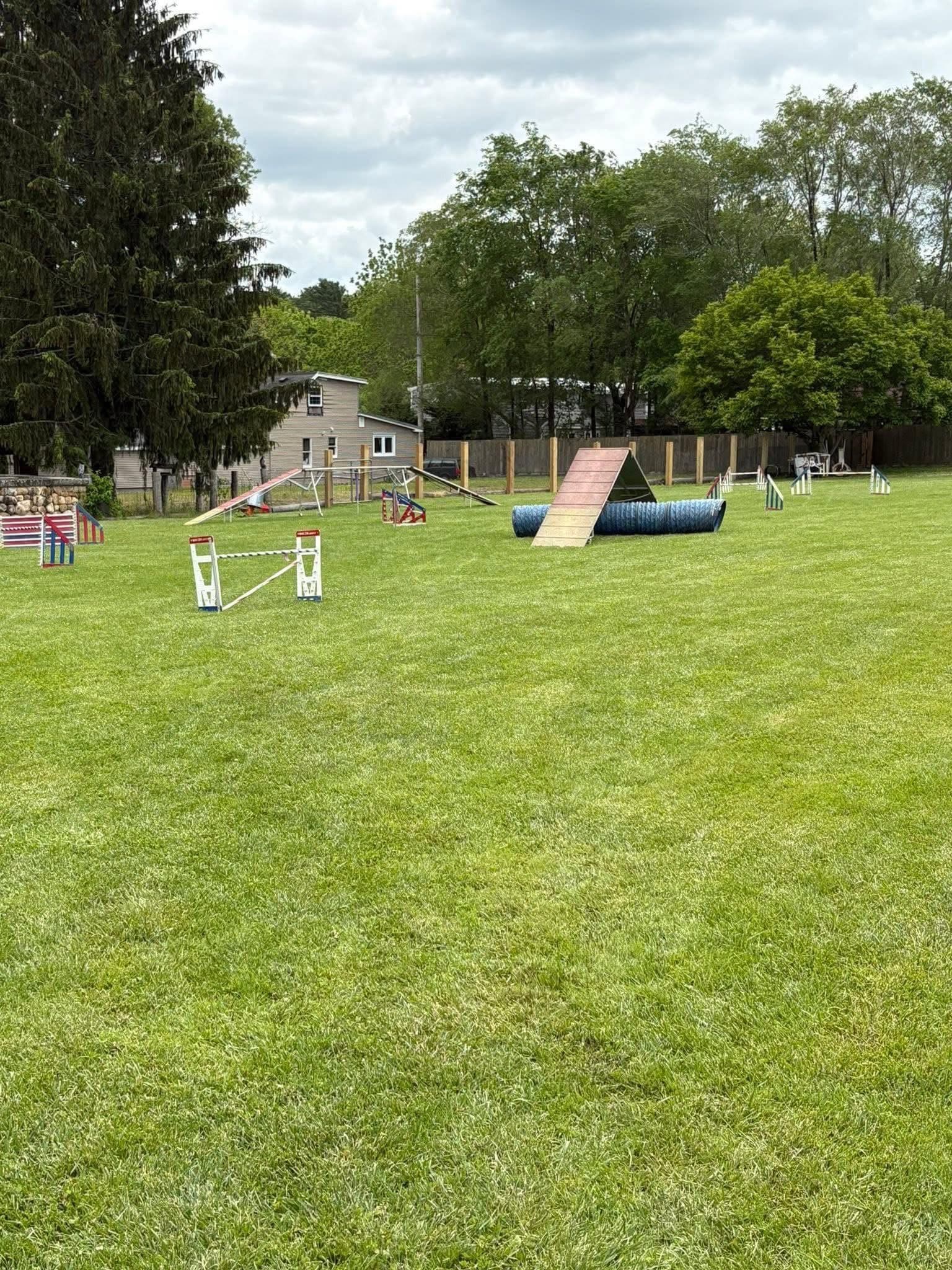 Outdoor dog agility training field in Acushnet with jumps, tunnels, an A-frame, and a teeter